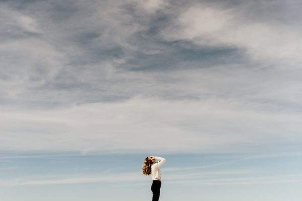 woman looking up to the sky while standing on white sand