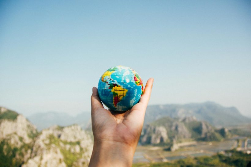 Person Holding World Globe Facing Mountain